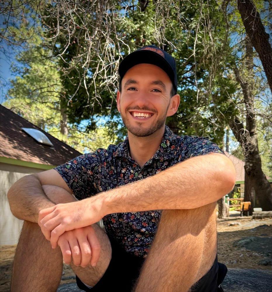 Jordan sitting on a granite boulder under pines, smiling